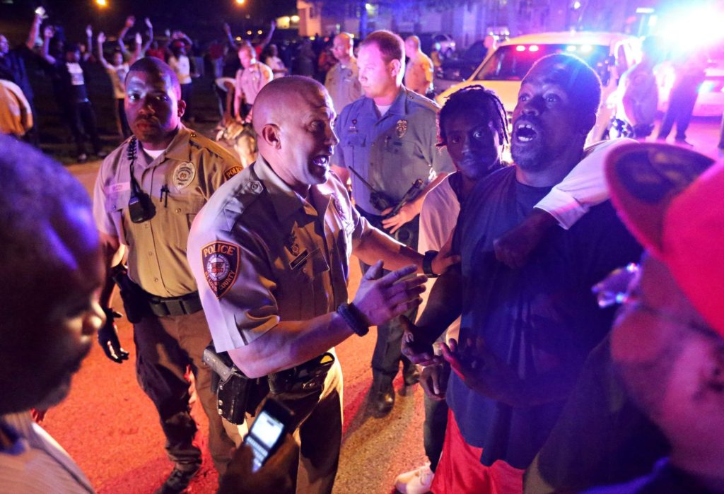 Police officers speak to a man as they try to break up a crowd in Ferguson, Mo., on Saturday, Aug. 9, 2014. Earlier in the day police had shot and killed an 18-year-old man.