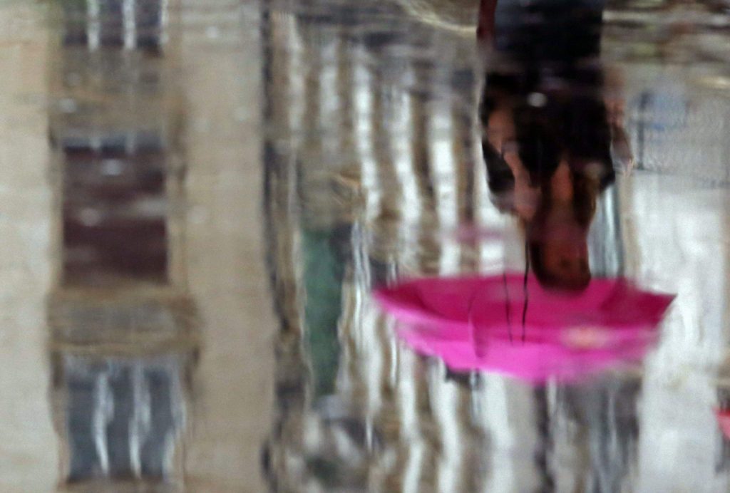 A woman is reflected in a puddle during heavy rain.